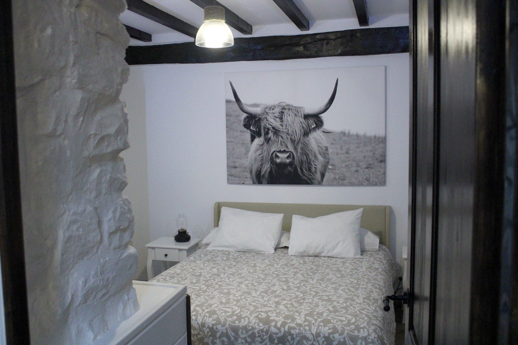 Cama de matrimonio bajo un gran cuadro de una vaca de las Highlands