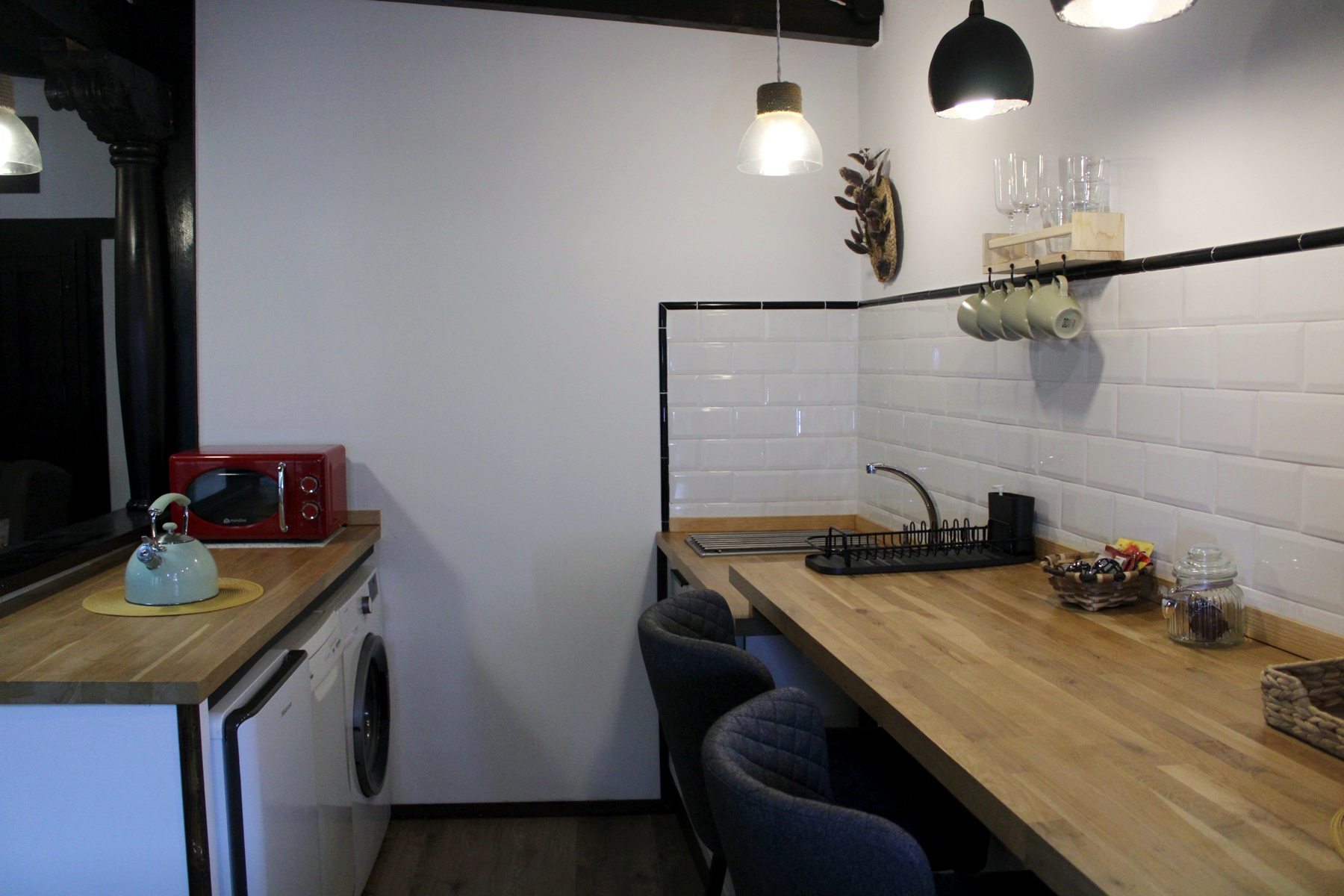 Barra de madera con dos taburetes, tazas colgadas y copas en la balda