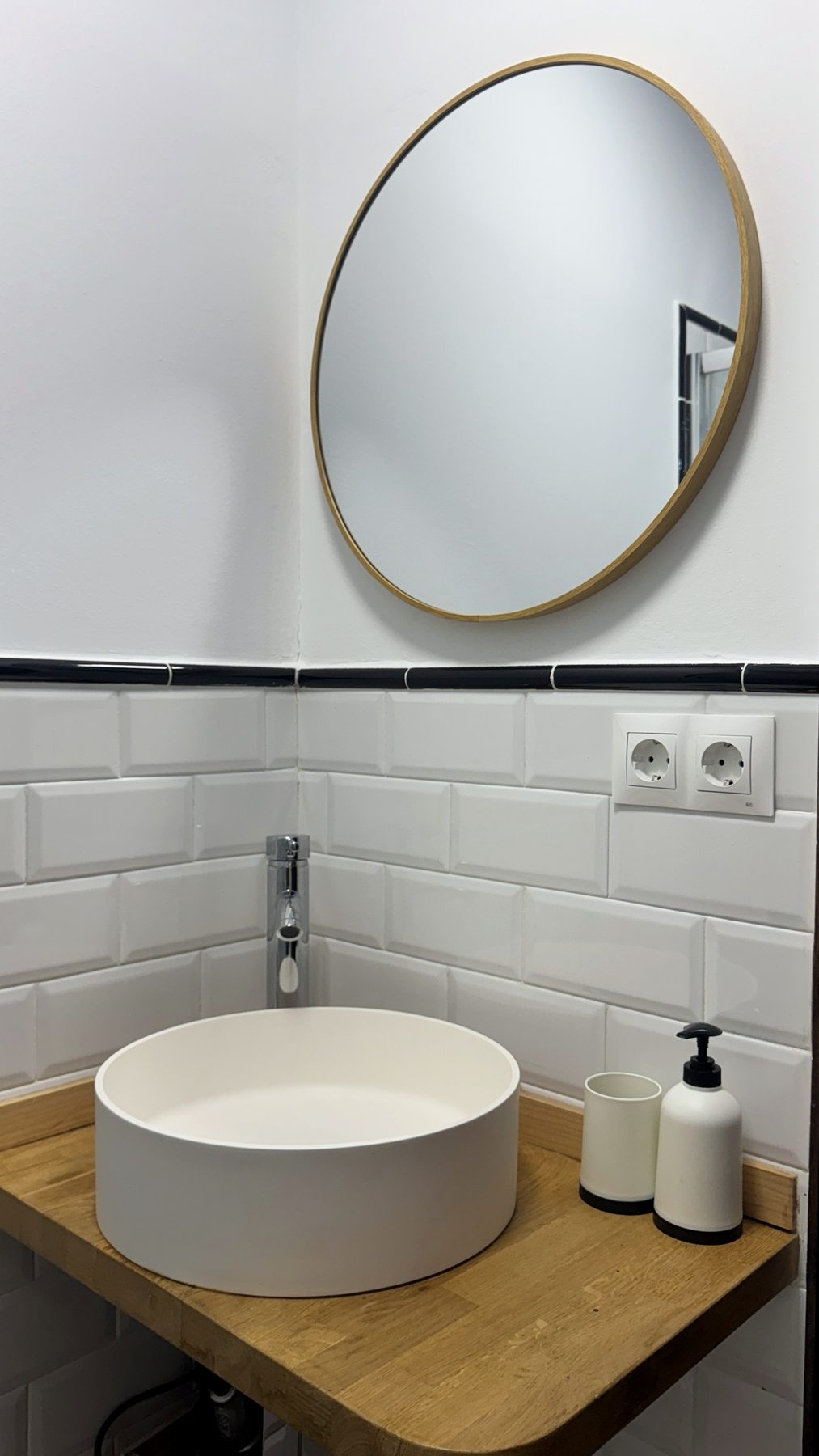 Lavabo redondo blanco sobre encimera de madera y espejo redondo