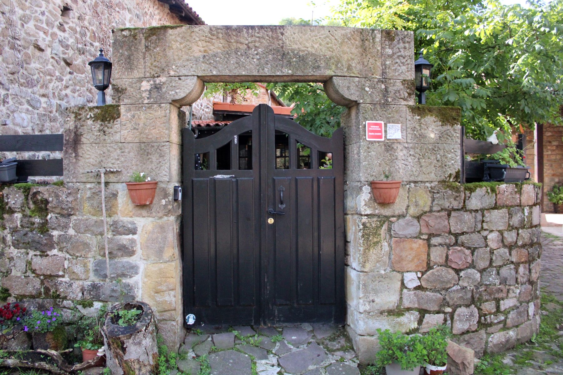 Puerta de madera negra bajo un arco de piedra, con macetas a los lados